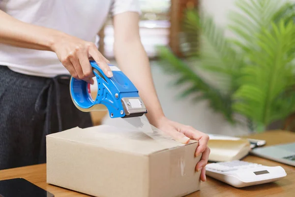 Online selling concept, Asian business women packing product into parcel box and sealing with tape.