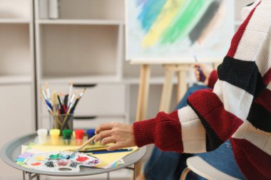 The art concept, Asian female artist smiling to happy while using brush to dip in color palette.