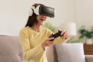 Eğlence aktiviteleri konsepti, VR gözlükleri ve joystick konsoluyla heyecan verici bir oyun oynayan genç kadın..