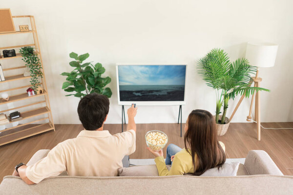 Relaxation concept, Couple holding remote control to changing channel and eating popcorn together.