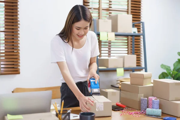 Online selling concept, Asian business women packing product into parcel box and sealing with tape.