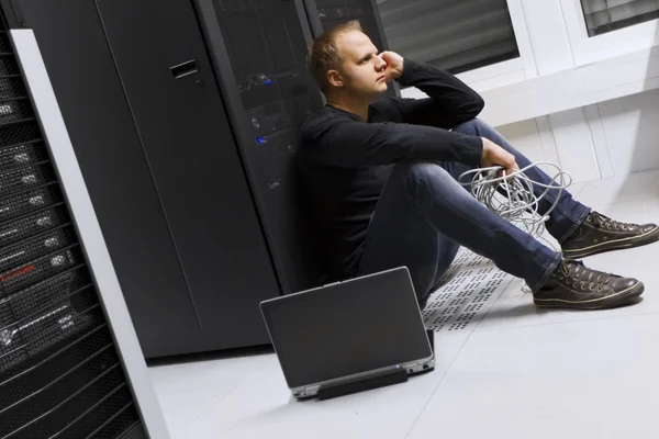 Frustriert und erschöpft sitzt er in einem Rechenzentrum. Apathisch vor einem Server-Rack sitzen. — Stockbild Ratgeber macht Pause — Stockfoto