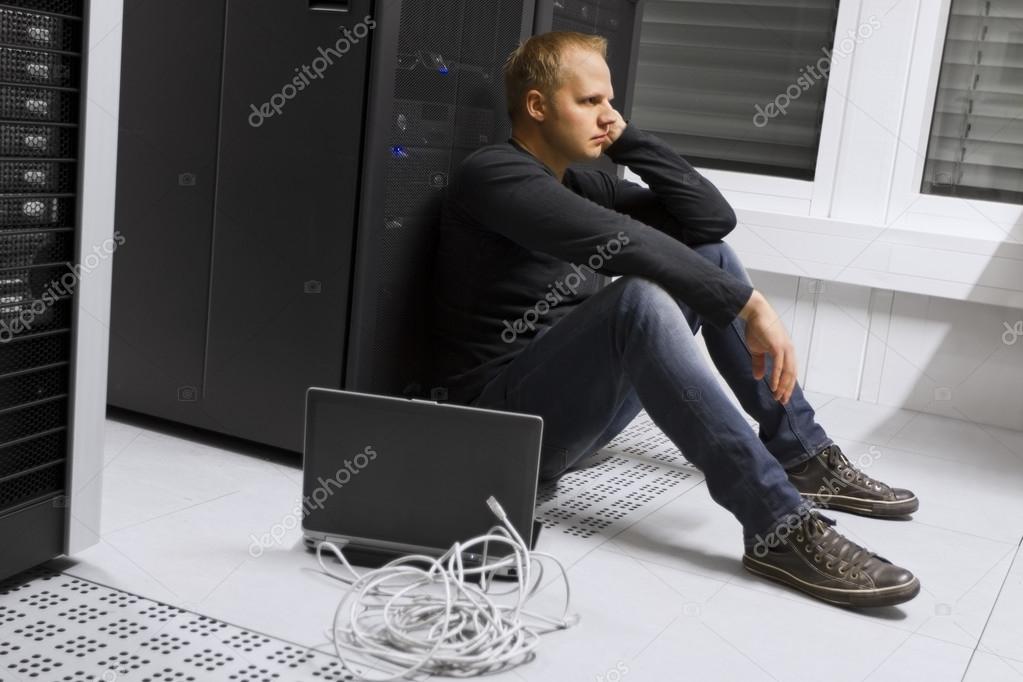 Herunterladen - Frustriert und erschöpft sitzt er in einem Rechenzentrum. Apathisch vor einem Server-Rack sitzen. — Stockbild Erschöpft im Rechenzentrum — Stockfoto