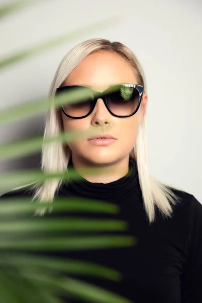 Hermosa mujer con gafas de sol escondidas detrás de hojas de palmeras tropicales — Foto de Stock