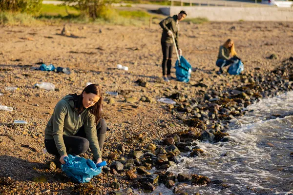 Mujer dedicada en un equipo recogiendo basura en bolsa en la playa —  Fotos de Stock