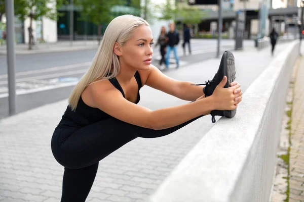 Mujer rubia hermosa y flexible estiramiento en la ciudad moderna —  Fotos de Stock
