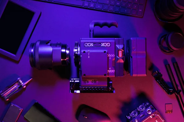 Overhead view of cinema camera and computer parts on colorful illuminated table — Stock Photo, Image