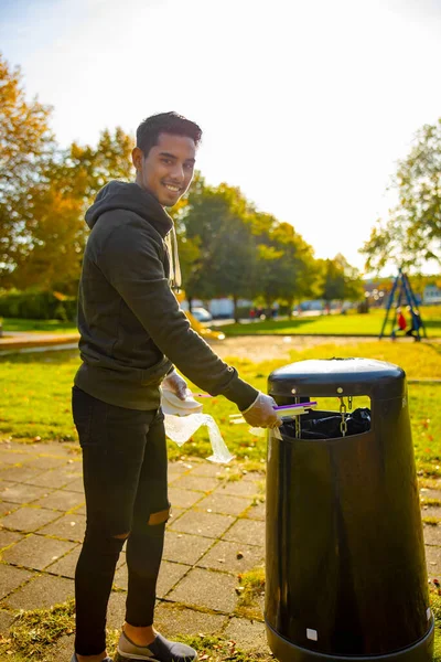 Sonriendo joven voluntario poniendo pajitas en cubo de basura en el parque — Foto de Stock