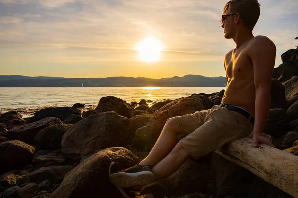 Junger Mann ohne Hemd sitzt bei Sonnenuntergang auf einem Felsen — Stockfoto