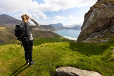 Yüksek dağlarda yürüyüş yapan ve Norveç, Lofoten 'deki Vestvagoy Adası' ndaki Haukland Sahili 'ne bakan bir kadın.