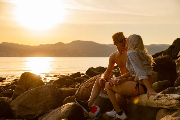 Jeune couple embrasser et boire de la bière tout en étant assis sur des rochers — Photo