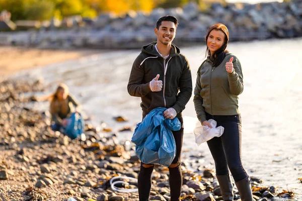 Two young volunteers showing thumbs up at beach — Stok fotoğraf