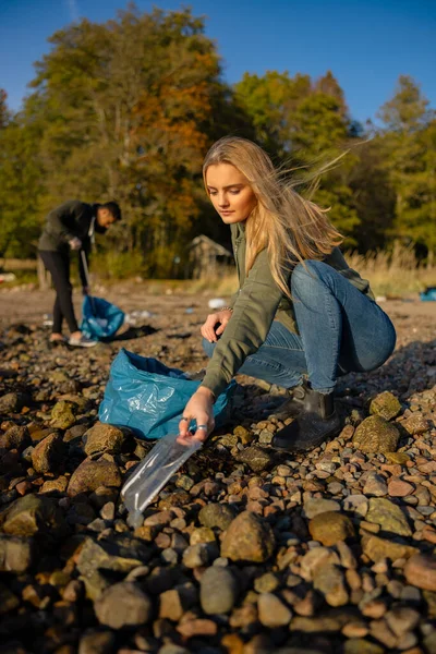 Junge Frau im Umweltschutzteam sammelt Plastik am Strand auf — Stockfoto