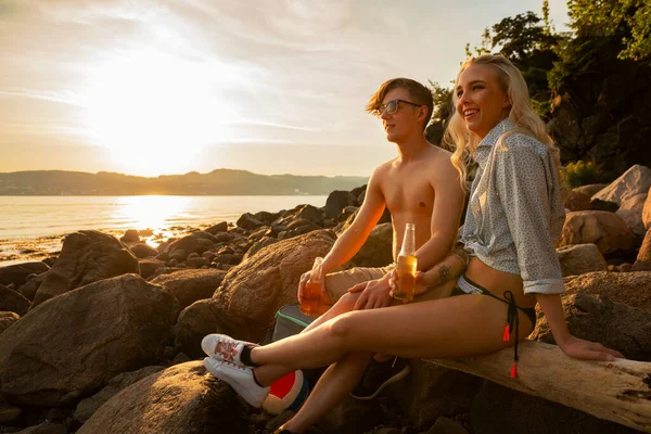 Souriant jeune couple tenant des bouteilles de bière à la plage — Photo