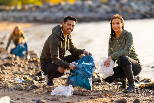 在阳光明媚的日子 一群尽心尽力 面带微笑的志愿者在袋子里捡塑料垃圾 男人和女人都在清理岩石海滩 他们在保护生态系统 免版税图库照片
