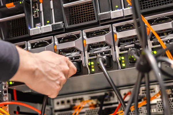 Close-up of hand of male technician plugging computer cable in SAN at datacenter