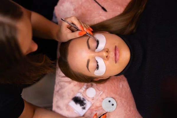 美容师使用镊子时正在进行睫毛扩张手术的漂亮女性患者的俯视图 — 图库照片