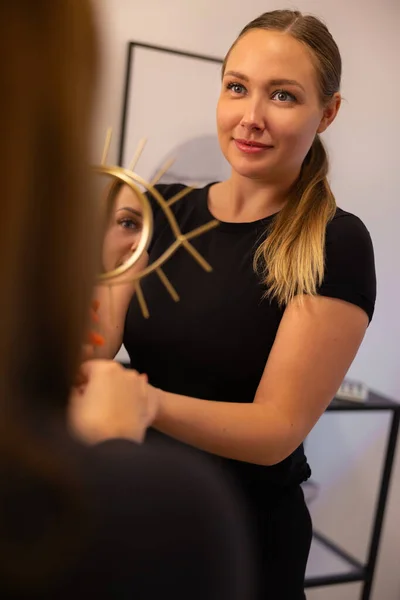 Glimlachende Jonge Schoonheidsspecialiste Houden Spiegel Voor Vrouwelijke Klant Kijken Naar — Stockfoto