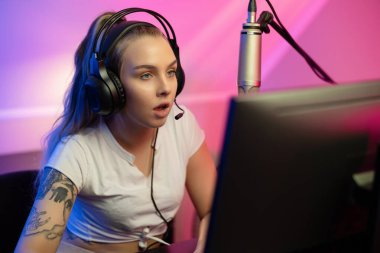 Bilgisayarında online video oyunu oynarken kulaklıkları olan odaklanmış bir e-sporcu kadın. Mavi ve pembe LED ışıkları olan oda.