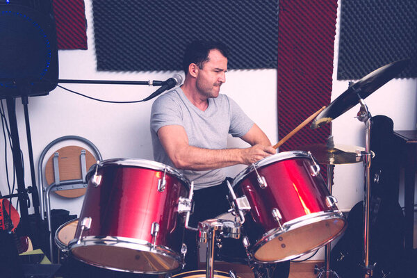 DRUMMER PLAYING HIS RED DRUMS WITH A LOT OF ENERGY IN HIS REHEARSAL ROOM