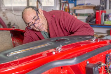 Emekli adam, boş zamanlarında kırmızı bir aracı tamir etmekten zevk alıyor ve kırmızı ceketini ve gözlüğünü burnunun ucuna takıp tek parça takmaya odaklanıyor..
