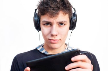 Kulaklarında büyük kulaklıklar ve elinde bir tabletle beyaz arka planda müzik dinleyip eğitime hazırlanan güzel bir genç.