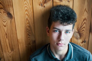 Güzel, cesur, üzgün, düşünceli görünüşlü bir ergen ahşap bir duvarın yanında oturuyor. Metin için yer