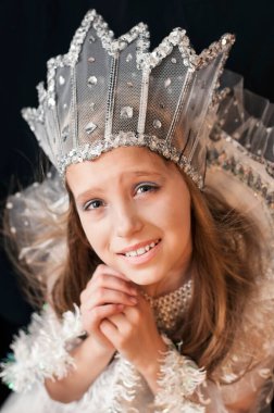 Karnaval kostümü giymiş, siyah arka planda kar kraliçesi kostümü giymiş bir kız. Bir şey soran bir bakış. Kar Kraliçesi karın düşmesini ister. Dikey