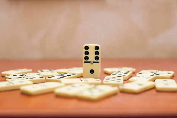 A domino game board is on a wooden table. All the dominoes lying on the table, only one domino stands, stands out from others. Domino is a game that can be played by the whole family