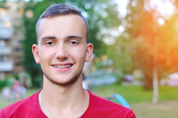 Portrait of a young man in nature who is resting, smiling and on his teeth, clearly sees the ceramic white braces. Copy space