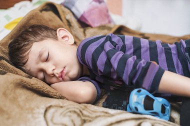Little boy sleeps sweetly in bed at home. Beside him are toys that the boy loves to play