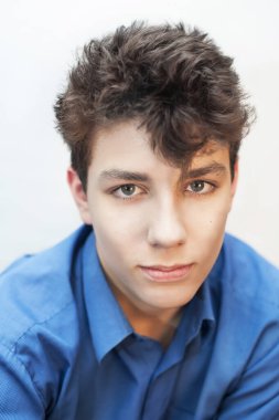 Portrait of a handsome young adolescent boy on a light background. It's time for this guy to go to the hairdresser because his hair sticks in different directions. Vertical