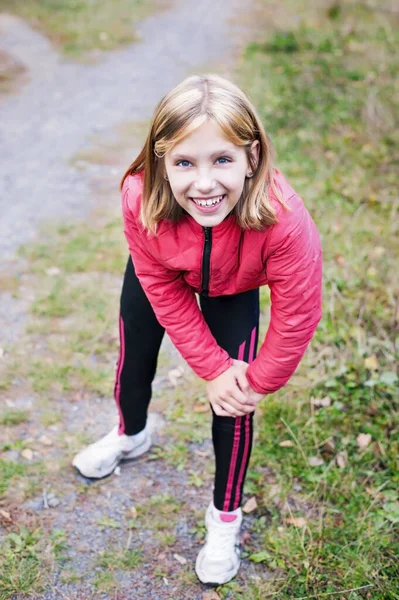 The girl in the nature is preparing for a morning jog. The girl is doing some physical exercises to warm up before running and smiling. Vertical
