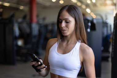 Genç bayan sporcu spor salonunda cep telefonunu izliyor.