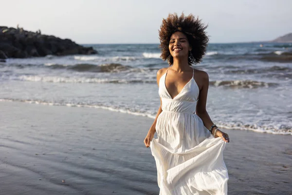 美しいです若いですアフリカの女の子で白いドレスは喜んでビーチに沿って実行 ストック画像