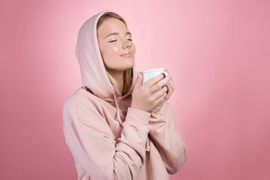 Sıcak bir içki iç, soğuk havada sıcak tut. Kapüşonlu genç bir kadın.