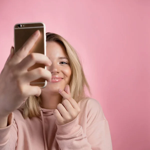 Jovem atraente em um capuz rosa usa um smartphone para comunicação de vídeo ou fotos. — Fotografia de Stock