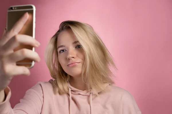 Jovem atraente em um capuz rosa usa um smartphone para comunicação de vídeo ou fotos. — Fotografia de Stock
