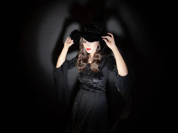 Strega alla festa di Halloween, una giovane bella donna bruna in un classico costume da strega con un cappello a punta. — Foto Stock