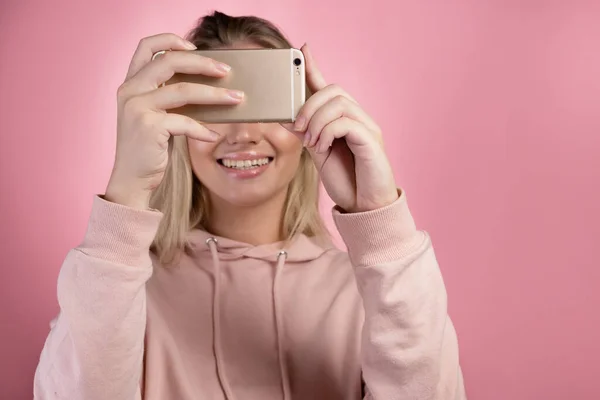 Jovem atraente em um capuz rosa usa um smartphone para comunicação de vídeo ou fotos. — Fotografia de Stock