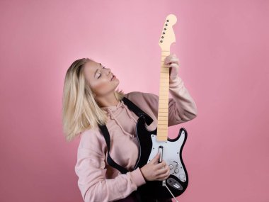 Genç ve çekici bir sarışın gülüyor ve oyuncak gitar çalıyor. Eğlence ve hobi..
