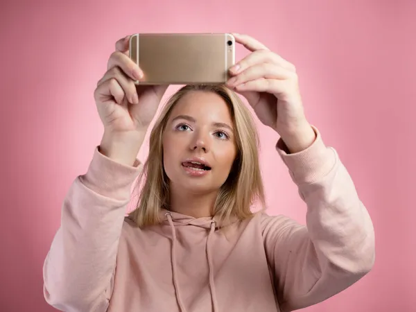 Uma jovem atraente com capuz rosa usa um smartphone para jogos móveis. — Fotografia de Stock