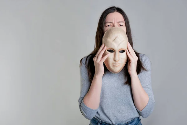 O femeie tânără ține o mască în mâini, ascunzându-și fața pe jumătate, o privire epuizată peste mască. — Fotografie, imagine de stoc