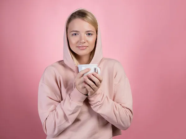 Užijte si teplý nápoj, mladá sladká žena v růžové mikině drží hrnek — Stock fotografie