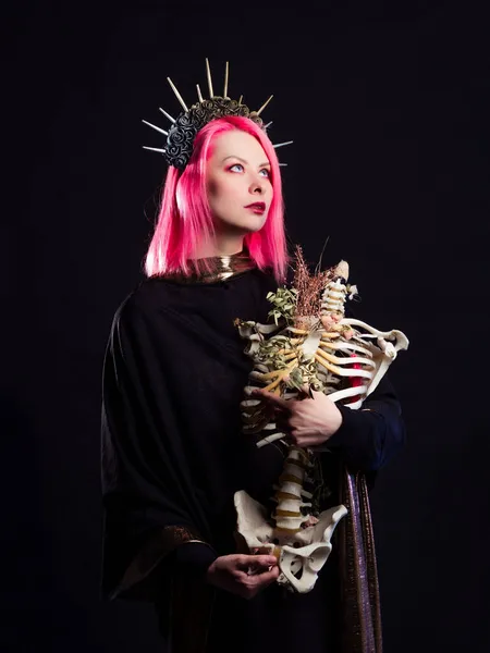A Gothic queen in a crown with roses and rays holds a skeleton of a man without a head in her arms.