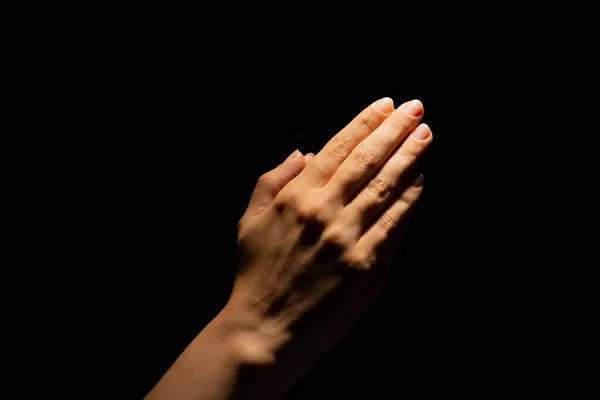Orando mãos sobre um fundo preto. Luz de cima. Mãos dobradas em oração. — Fotografia de Stock