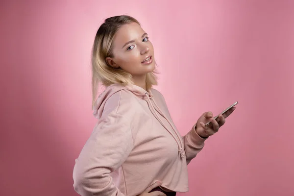 Navegação na Internet, aplicações móveis. Uma jovem atraente em um capuz rosa usa um smartphone. — Fotografia de Stock
