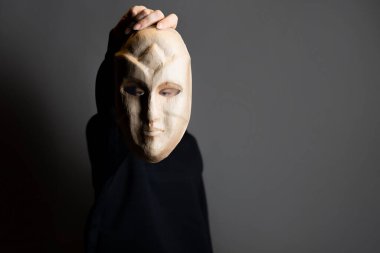 Maskenin arkasına saklanan koyu renk kapüşonlu genç bir kadın yüzünü maskeyle gizliyor.,