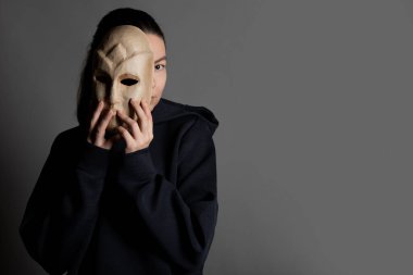 Maskenin arkasına saklanan koyu renk kapüşonlu genç bir kadın yüzünü maskeyle gizliyor.,