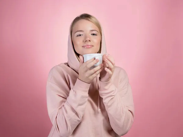 Desfrute de uma bebida quente, uma jovem doce mulher com um capuz rosa segura uma caneca — Fotografia de Stock